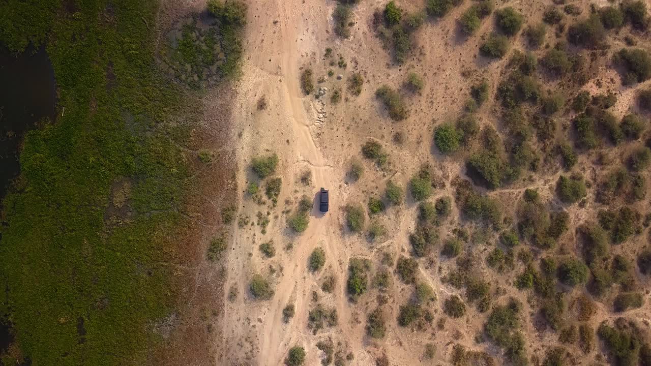 Overhead drone shot showing a 4x4 safari vehicle traversing tracks through semi-arid, bushy land on the edge of the Nile river wetlands in Murchinson Falls NP, Uganda, Africa
