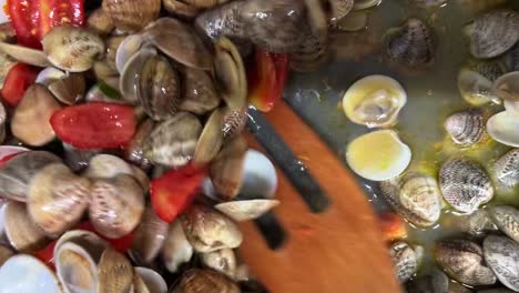 agitando deliciosas almejas frescas y tomates con tenedores de madera en sartén caliente