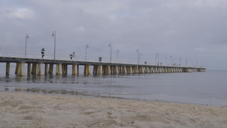 People-Walking-on-Orlowo-Pier-in-Slow-Motion-on-Cloudy-Winter-Day-in-the-coastal-borough-of-Gdynia,-Poland