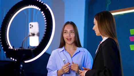 a couple of ladies speak in front of camera. women are recording video for a blog using ring light.