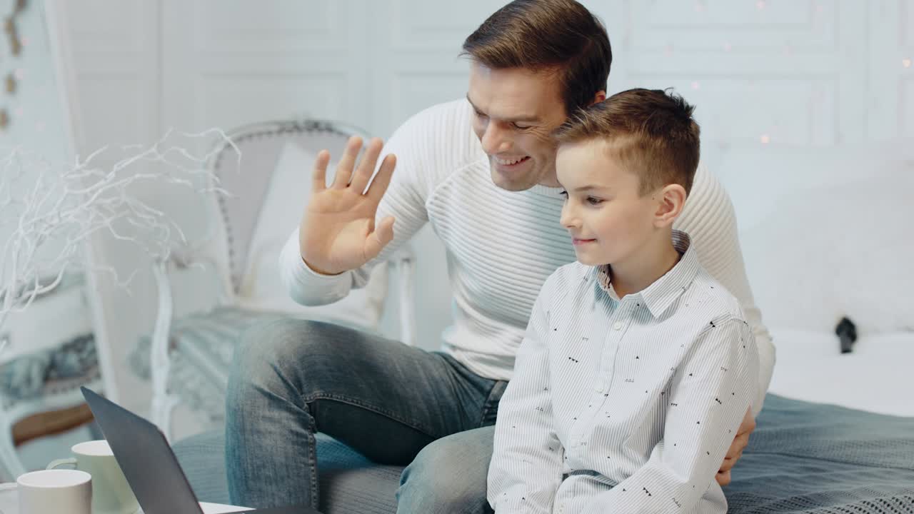 padre sonriente e hijo charlando en una computadora portátil en una casa de lujo.