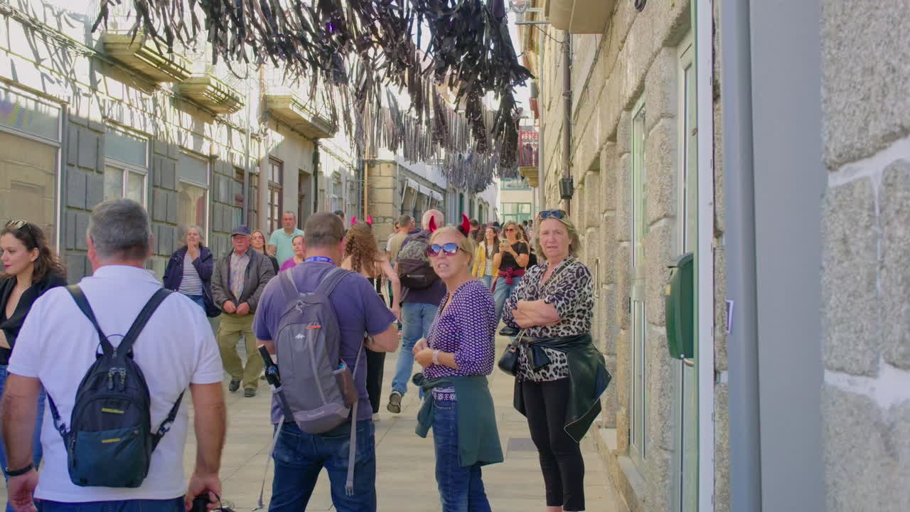 People walking on a narrow, historic street with decorations hanging from above
