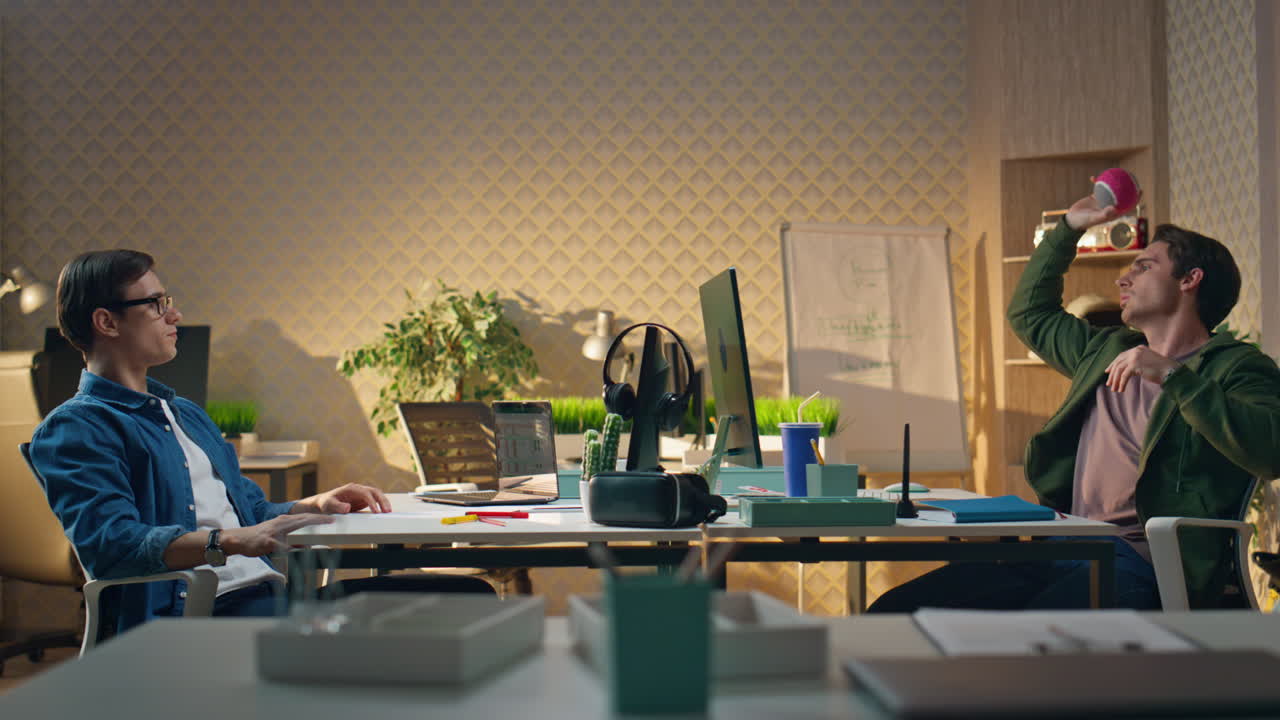 편안한 동료들이 공을 던지고 사무실에서 놀고 두 명의 스타트업이 함께 휴식을 취하고 있습니다.