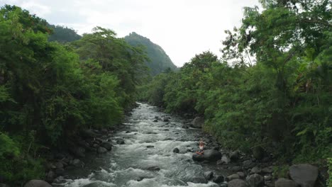 Lowering-into-lush-jungle-with-river-and-woman-in-Lotus-Arm-extended-pose-on-rock