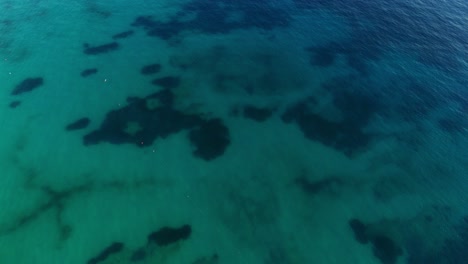 crystal-clear turquoise waters with subtle dark patches and distant boats, aerial view