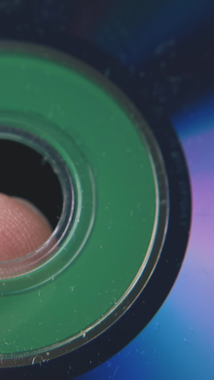 young man holds round shining compact disc on finger with grooves in dark background extreme close view