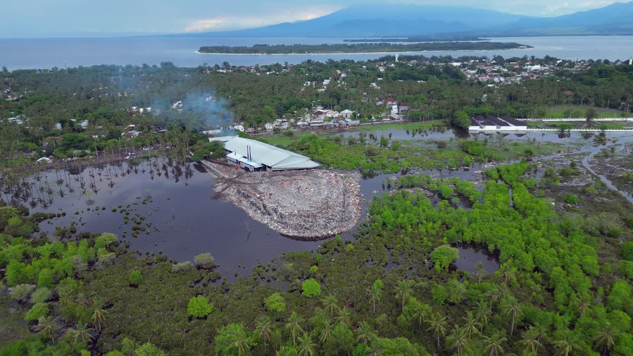 Vuilstortplaats die zich uitstrekt vanaf een industrieel gebouw, donker water en omringende mangroven vervuilend, wat milieuvervuiling toont. Unieke luchtfoto, omgekeerde panorama dronevlucht.