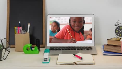 Animation-of-a-laptop-with-a-mixed-race-child-writing-in-a-notebook-in-a-classroom-on-the-screen