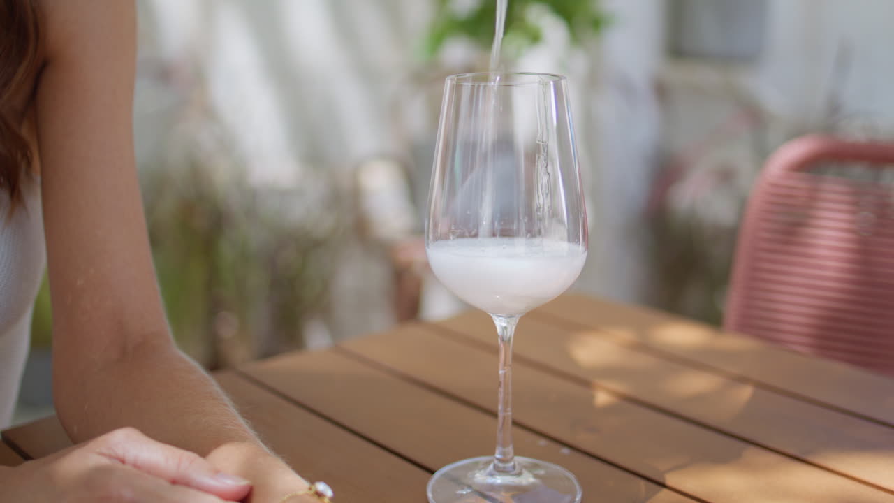 Primo piano di vino versato in un bicchiere dalle mani di una donna al tavolo di un caffè. Signora elegante che attende la sua bevanda.