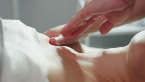 close up of beauty expert smoothing female client chest with fingertips in circular massage motions relaxing spa treatment under soft clinic lighting on white linen table beside skin care trolley