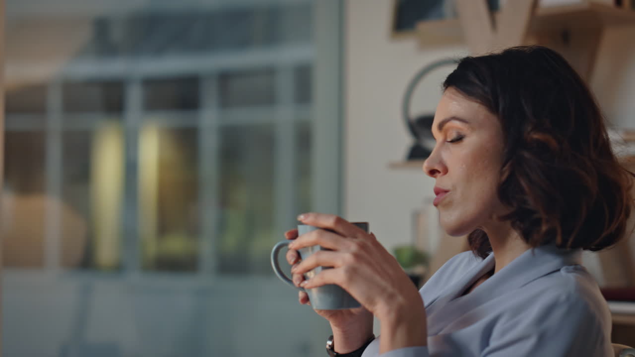 Nærbillede af kvindelig direktør, der drikker kaffe på et mørkt kontor. Leder holder pause.