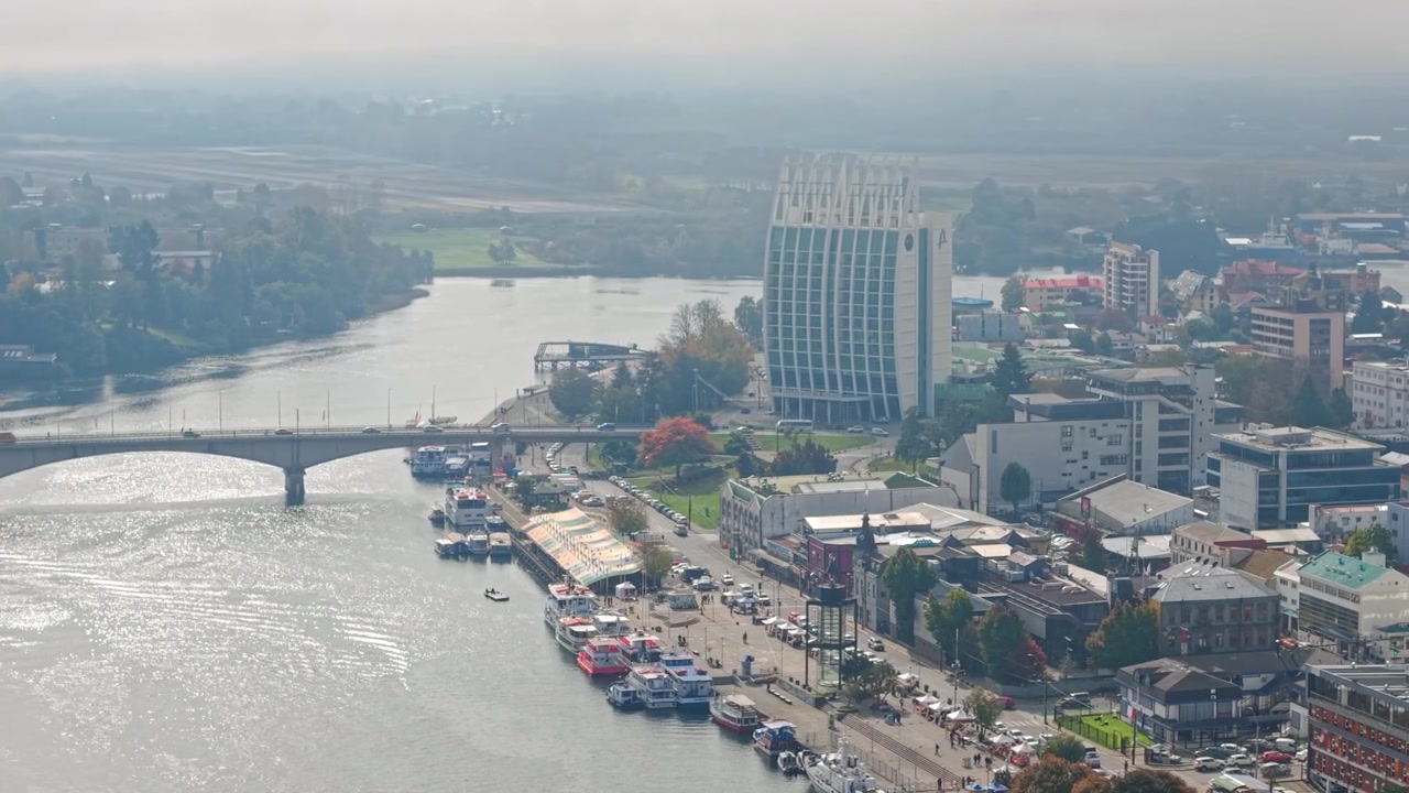 Orbita con teleobiettivo sul centro di Valdivia, Cile, con la sua fiera fluviale, il Ponte Pedro de Valdivia e il Dreams Hotel, avvolti in una leggera nebbia all'alba