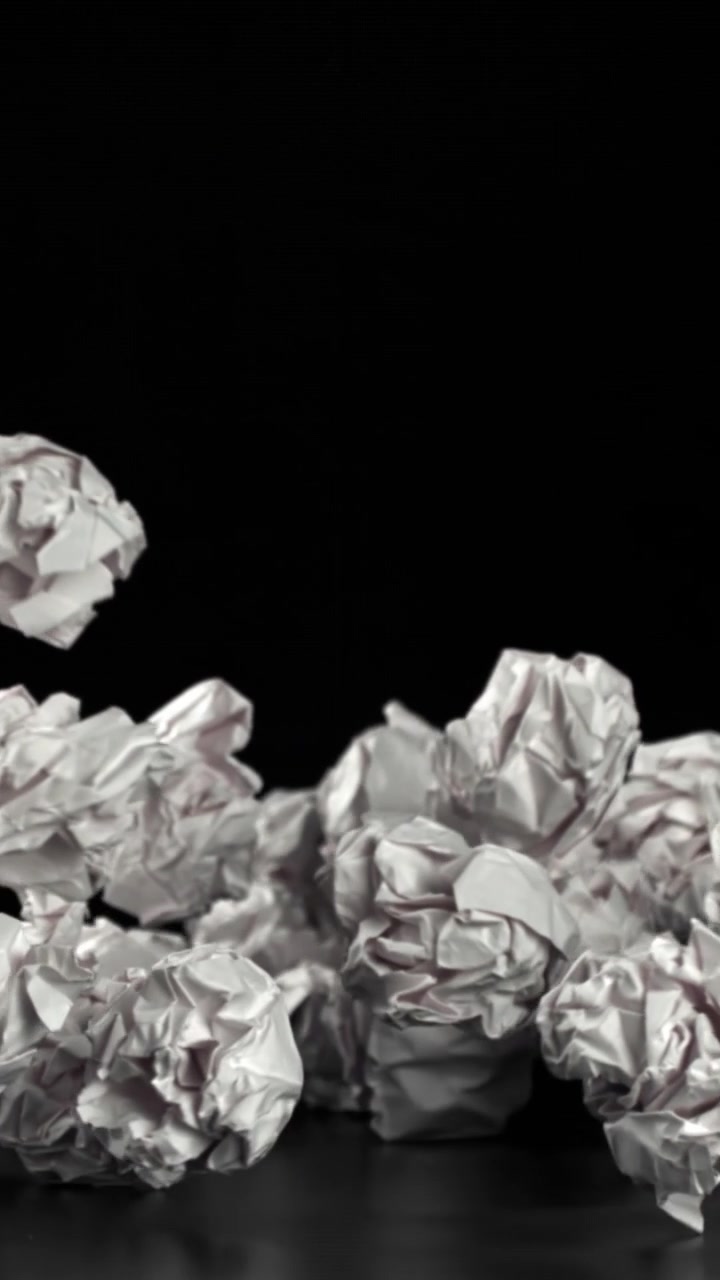 Palline di carta bianca accartocciata che cadono e si accumulano su sfondo nero