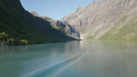 boat sailing in lyngen fjord with rocky mountains of scandinavian alps in background on sunny day, norway