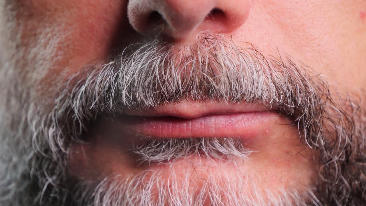 A bearded man with a mustache exhales a cloud of smoke from a cigarette through his nose