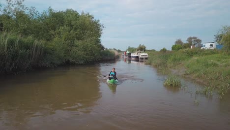 Hombre-En-Kayak-Hacia-La-Cámara-En-El-Río-Con-Juncos-Y-árboles-En-Las-Orillas