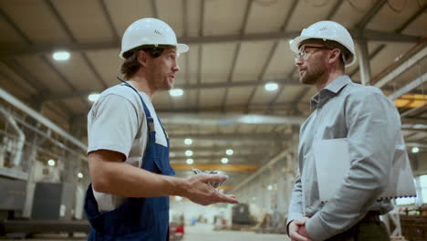 engineer shaking hands with mechanic, instructing him at work in factory