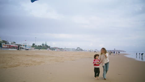 happy mother launching kite toy with adorable son on autumn beach together.