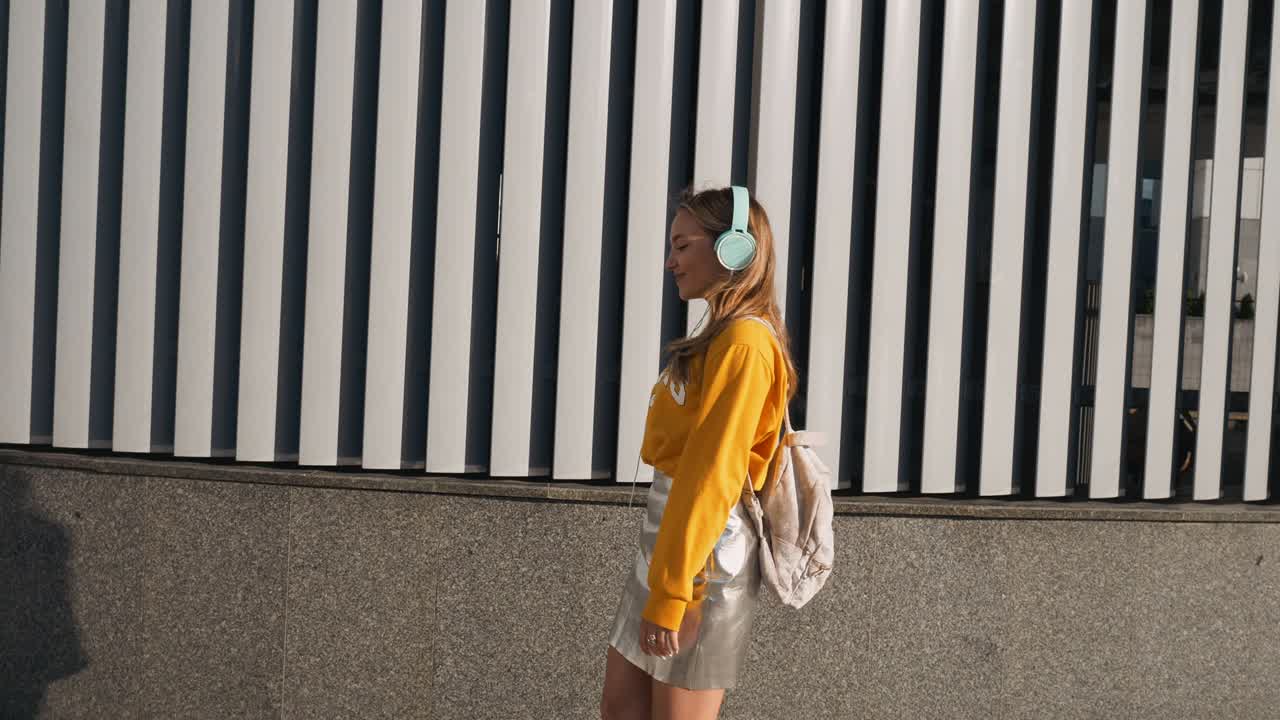 retrato de una joven linda y atractiva en el fondo urbano escuchando música con auriculares. mujer con blusa amarilla y falda plateada