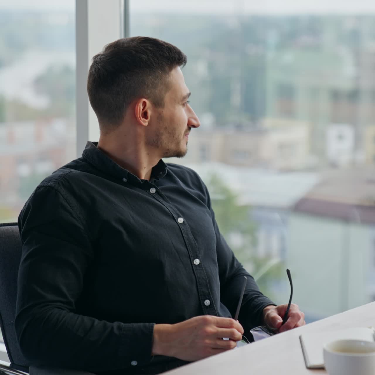 Caucasian man working on laptop and takes off his glasses leaning backwards in chair. Male employee looks at window having a break from work