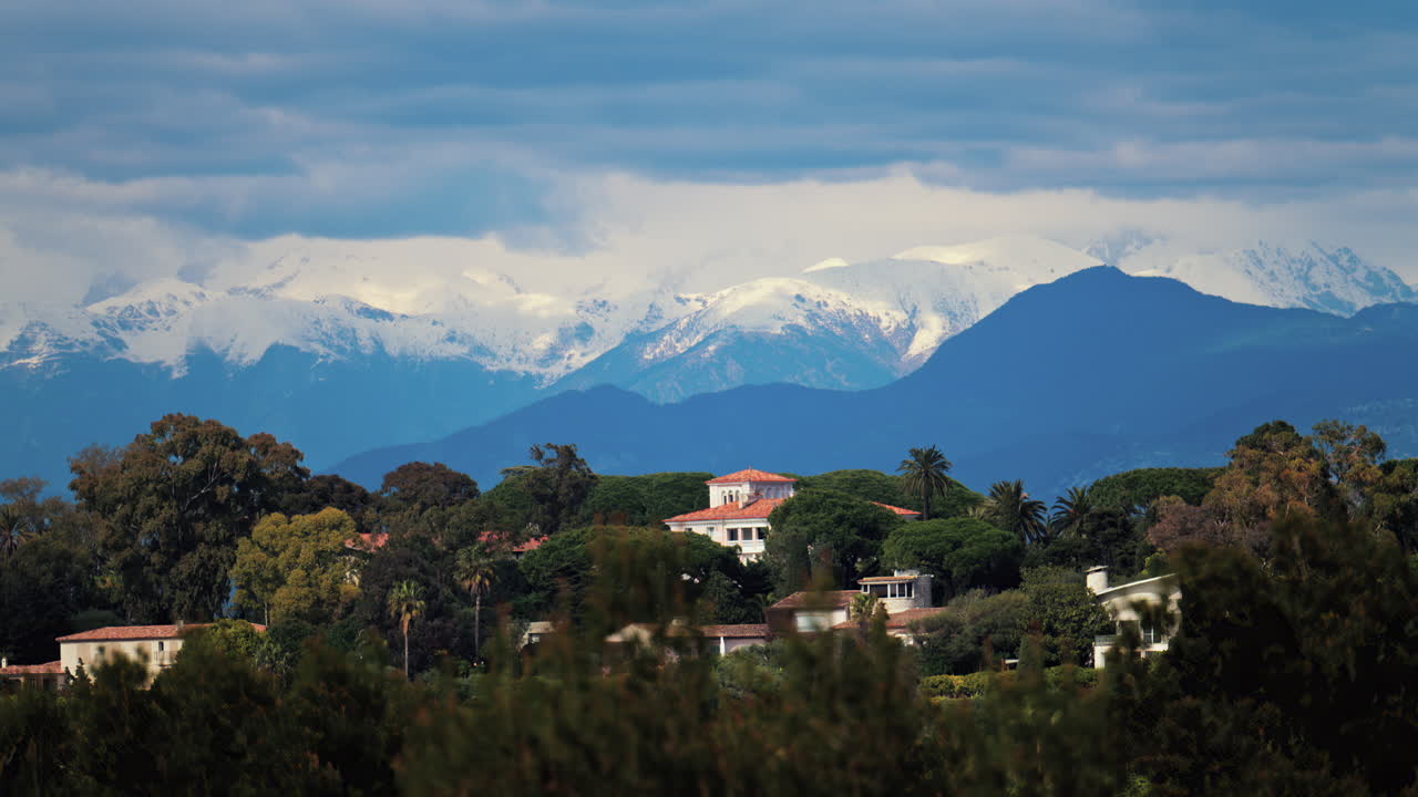 Distant view of orange villas surrounded by green trees with the mountains on the background on a cloudy day