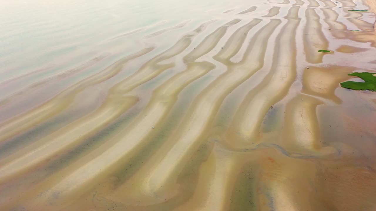 Cape Cod tidal flats at low tide reveal long sand ridges, shallow pools of seawater reflecting the sky, and dune grass bordering the beach in a timeless New England coastal scene
