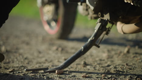 close-up of a biker removing the kickstand of the motorcycle, as she drops one leg for, the front tire is slightly turned to the left, while the background and foreground are blurred