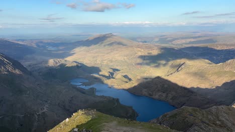 Scenic view from Y Garn summit in Snowdonia National Park showing mountain peaks, deep valley, rocky slopes and clear lake under partly cloudy sky, captured while hiking along trail.