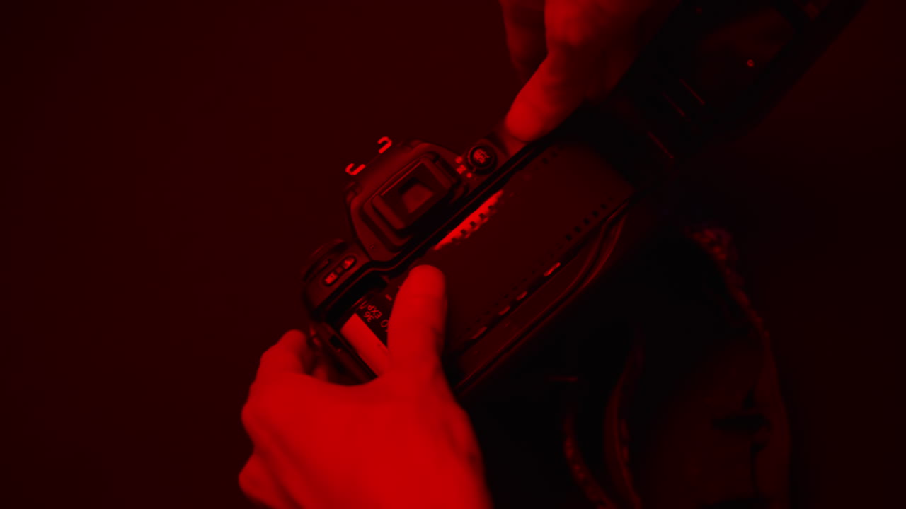 Close-up of hands holding a vintage film camera under red darkroom lighting. Retro photography mood with cinematic atmosphere, perfect for creative, nostalgic, or artistic visuals
