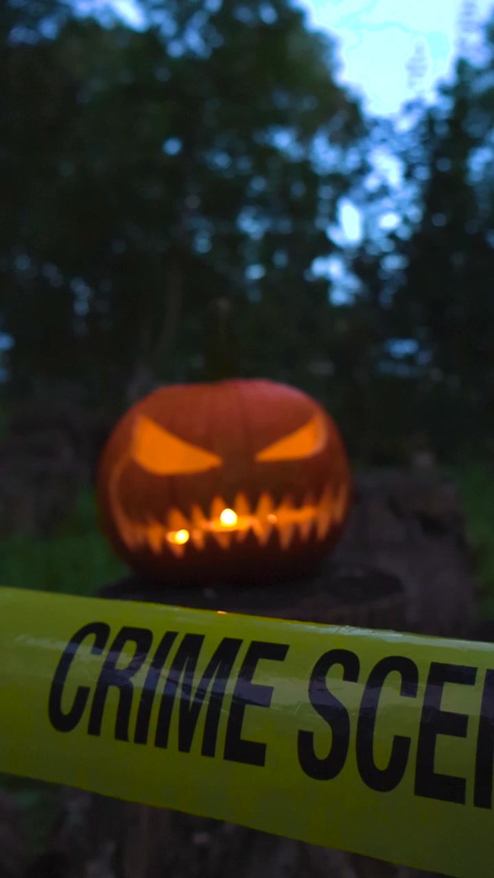 Creepy glowing Jack o' lantern with a sinister face sitting in a dark forest at dusk, with yellow police caution tape marking a crime scene in the foreground for a spooky concept