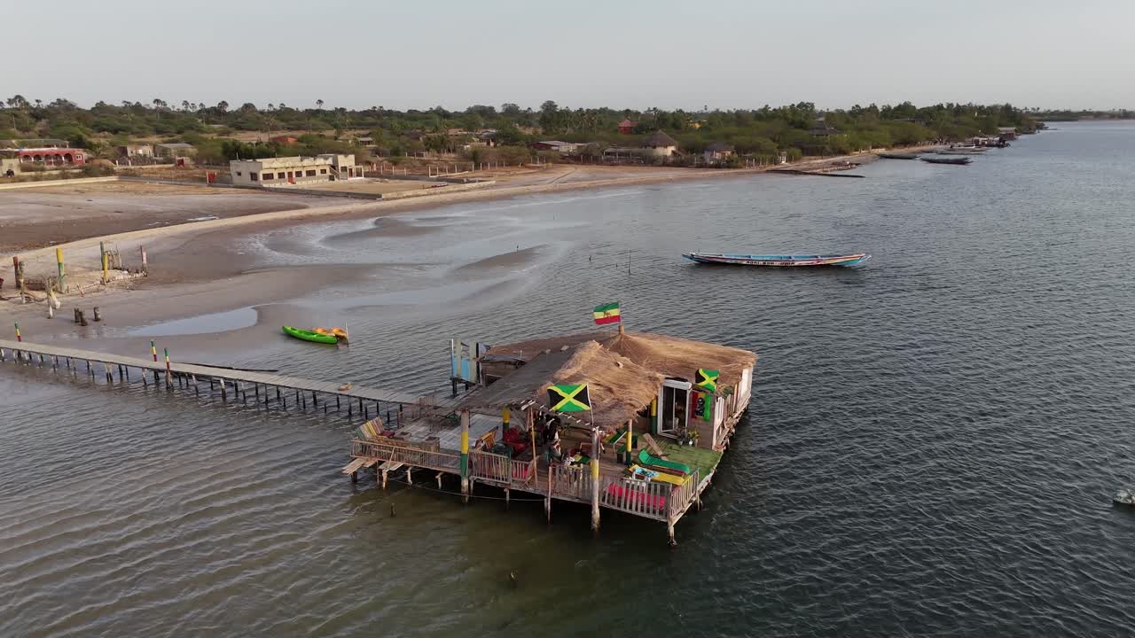 Aerial drone footage of a ferry docked at a riverside village in Sine Saloum Delta, Senegal. Scenic cultural landscape with boats, houses and waterfront