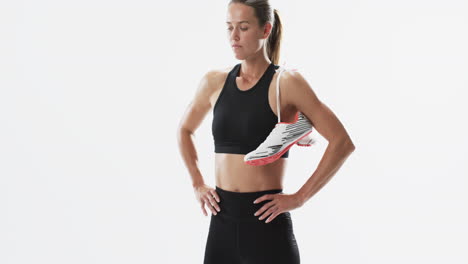 joven atleta mujer caucásica sostiene zapatillas de correr en un fondo blanco