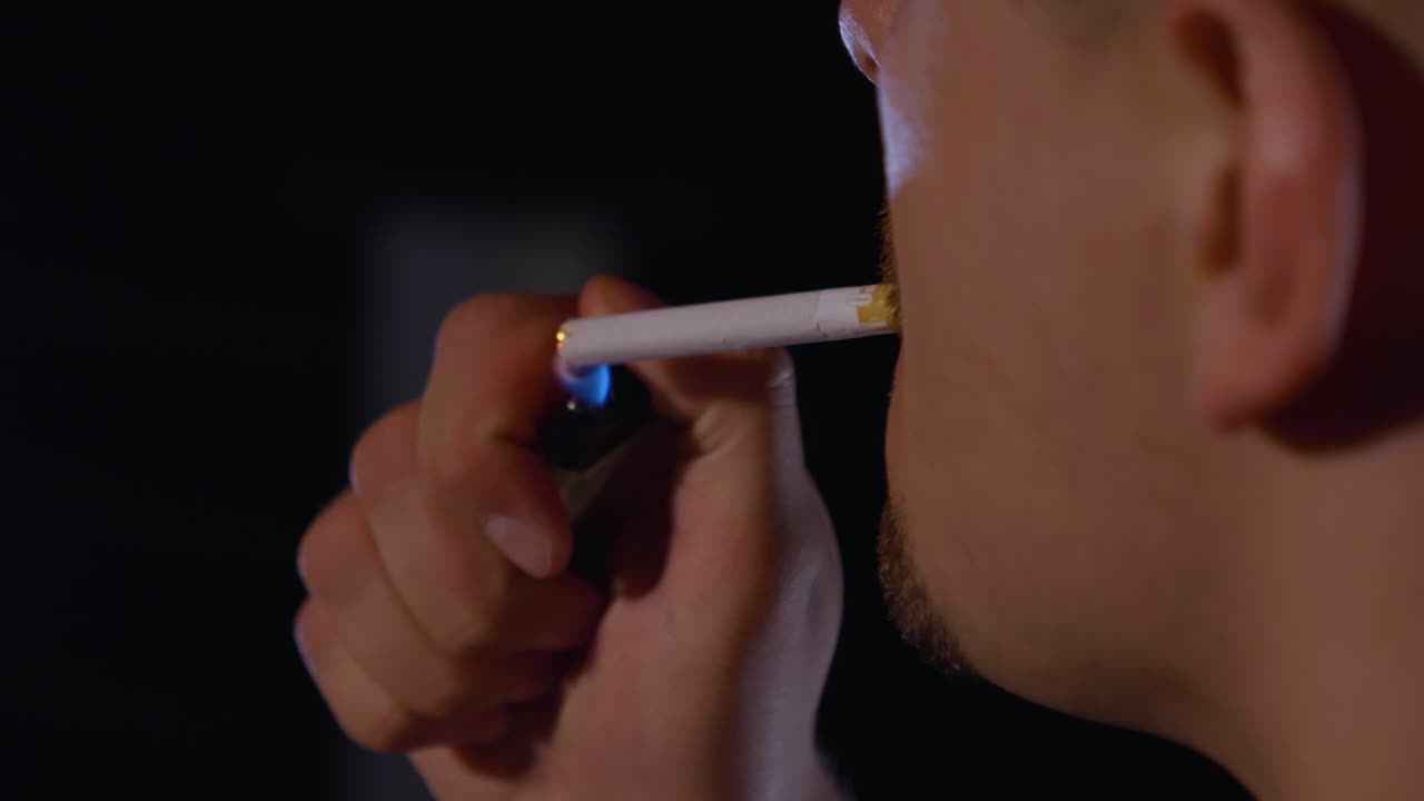 primer plano de una persona encendiendo un cigarrillo por detrás con un fondo negro, cámara lenta
