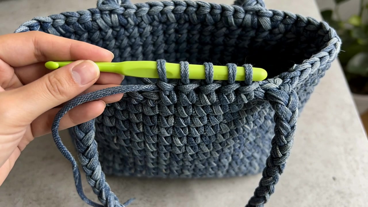 Una mano che aggancia gli anelli, tirando il filo attraverso il bordo del cestino a casa, e finendo il punto del bordo con un uncinetto verde.