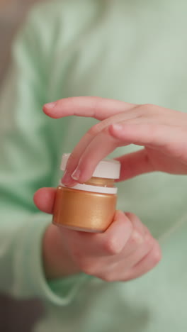 little child in green sweatshirt opens bottle with golden paint sitting on sofa in living room closeup slow motion. girl preparing for art lesson