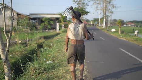 man with a fork hoe walking down a road