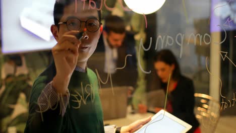 male executive writing on glass board while using digital tablet in office 4k