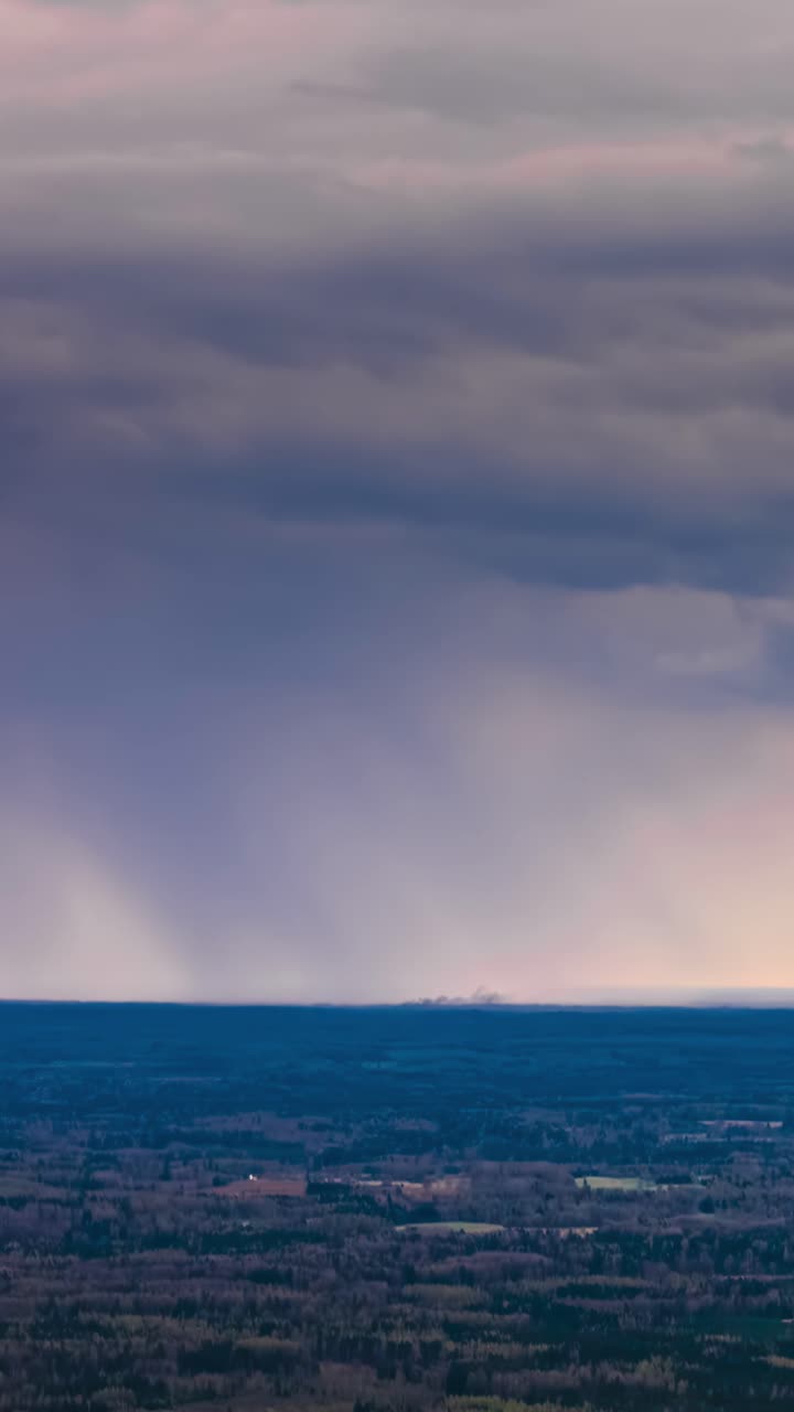 Vertical aerial time lapse shows dramatic storm clouds and rain moving across the sky during blue hour over the dark rural countryside of Latvia
