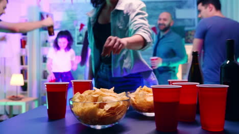 Mujer-Joven-En-Una-Fiesta-Con-Luz-De-Neón-Tomando-Patatas-Fritas-De-La-Mesa-Y-Una-Taza-De-Cerveza.