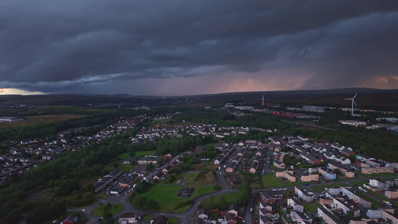 Stormy sunset sky and distant rain over a Welsh town with wind turbines