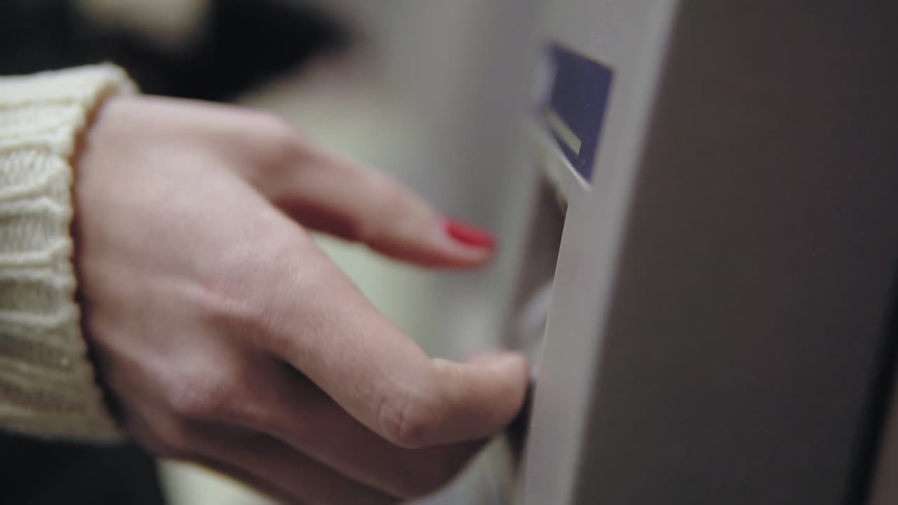 Woman's hand with painted red nails inserting credit card to ATM. Beautiful manicure