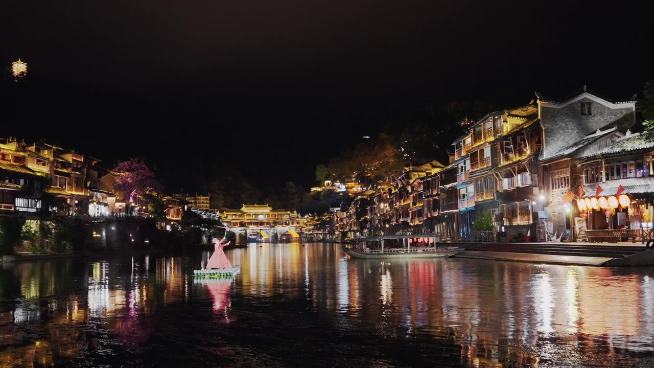 Luzes noturnas panorâmicas de festival no rio, vista grande angular de uma cidade histórica à beira-rio iluminada por cordões de lanternas e luzes de edifícios, carro alegórico cerimonial rosa flutuando perto do centro, cintilante.