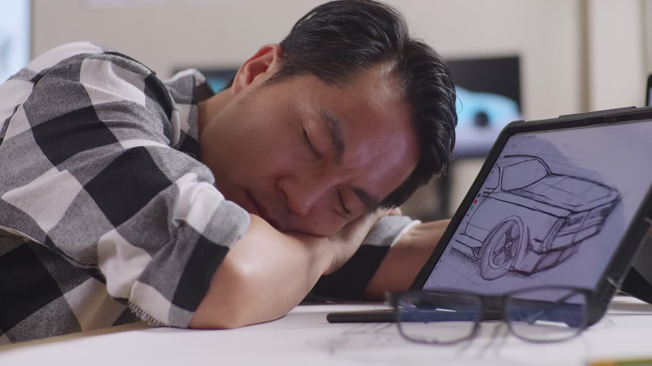 Close Up Of Asian Male Sleeping While Drawing New Car Design Concept On A Tablet In The Studio With Tv And Computers Display 3D Electric Car Model