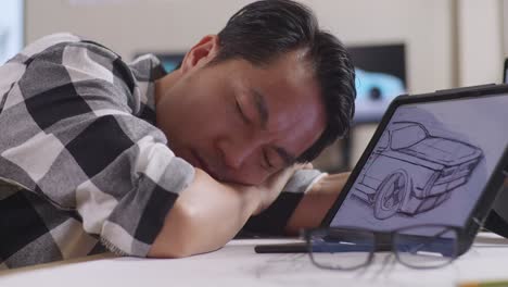 close up of asian male sleeping while drawing new car design concept on a tablet in the studio with tv and computers display 3d electric car model