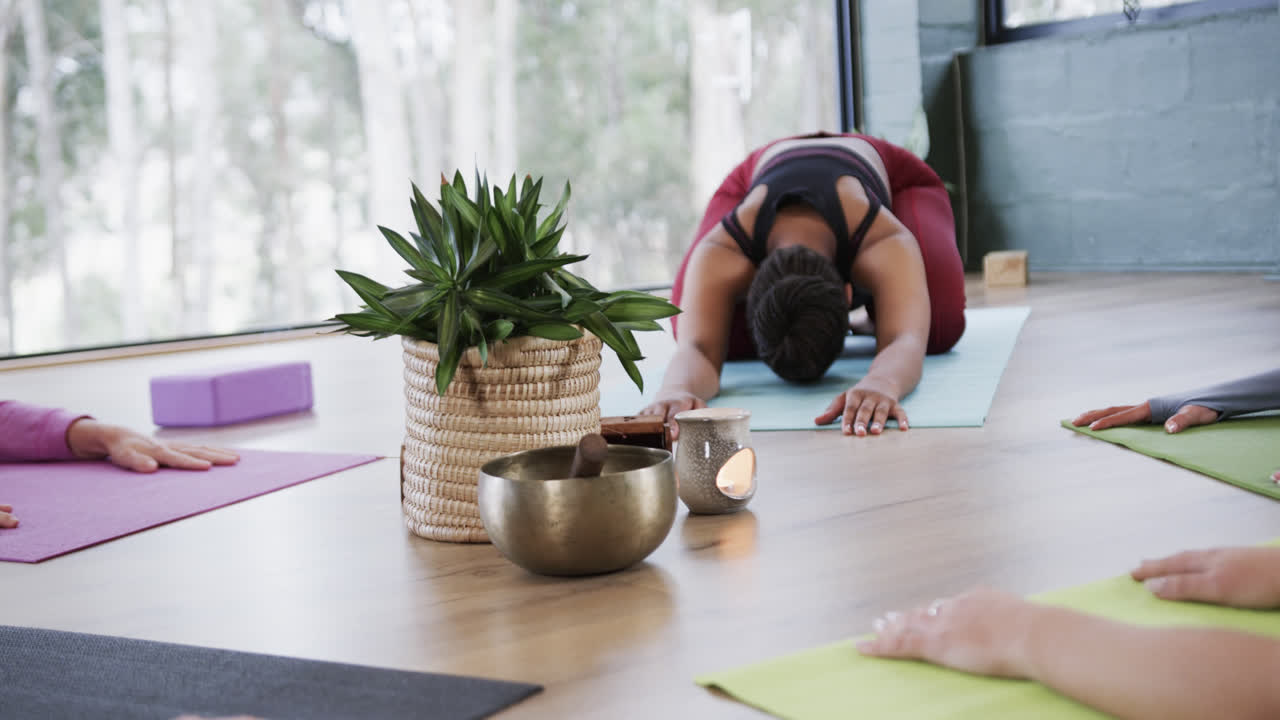 mujeres diversas practicando poses de yoga infantil alrededor de plantas y cuenco de canto en el estudio