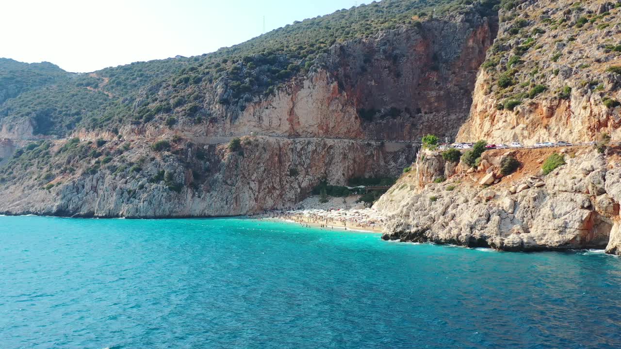 Aerial drone panning in at Kaputas Beach in Kas Turkey on a sunny afternoon day during summer as European tourists sun bathe surrounded by beautiful blue Mediterranean Sea and Mountain Cliffs