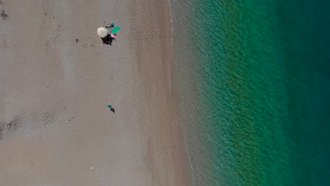 Tranquil-beach-with-few-umbrellas-on-sand-near-emerald-turquoise-sea-water-in-Mediterranean