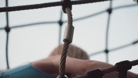 young girl climbing rope net structure in park playground at sunset, showcasing determination, balance and adventurous spirit as she navigates climbing frame under soft evening sky