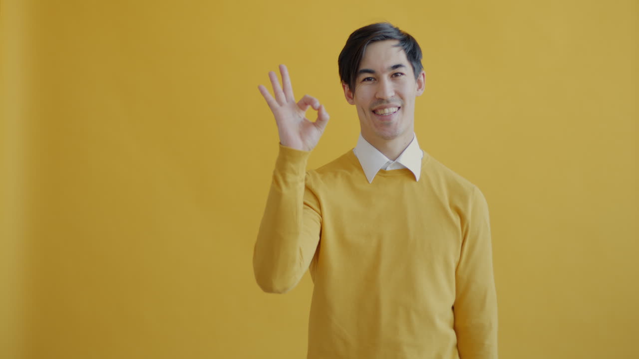 Man in a yellow sweater gesturing 'okay'
