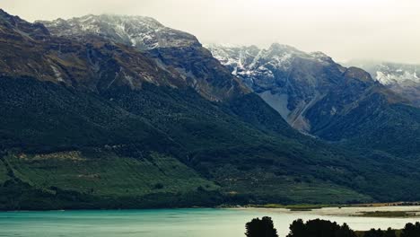 Misty-layer-of-clouds-across-snow-capped-mountains-overlook-calm-waters-in-New-Zealand